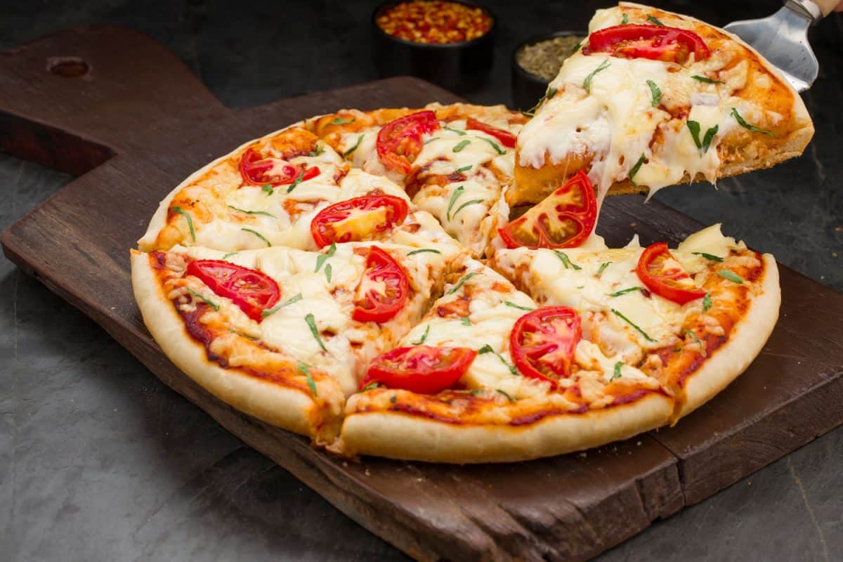 用番茄、罗勒叶和马苏里拉奶酪做馅料，铺在薄酥皮上，放在木板上，自制美味披萨