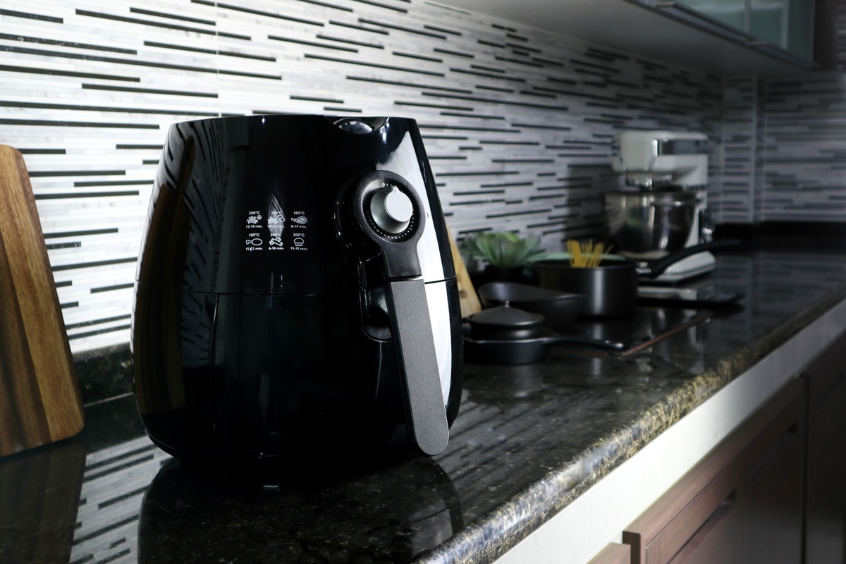 一个黑色的油锅或无油炸锅，空气炸锅设备，在漂亮的室内设计厨房的黑色大理石桌子上。bd手机下载