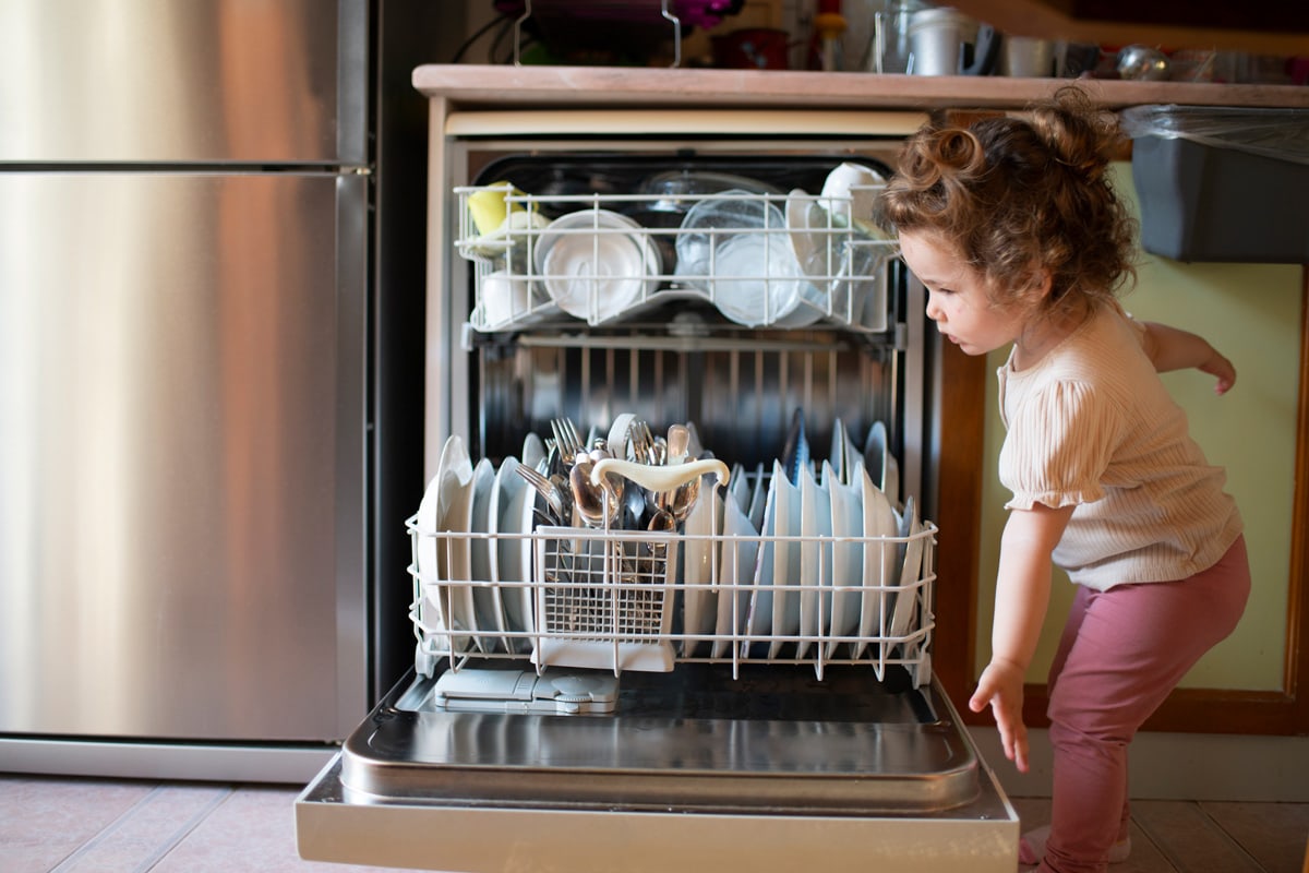 为了帮助蹒跚学步的孩子、女孩、妈妈，把脏盘子放进家里的洗碗机里。可爱的小女婴洗碗机，概念水的重要性