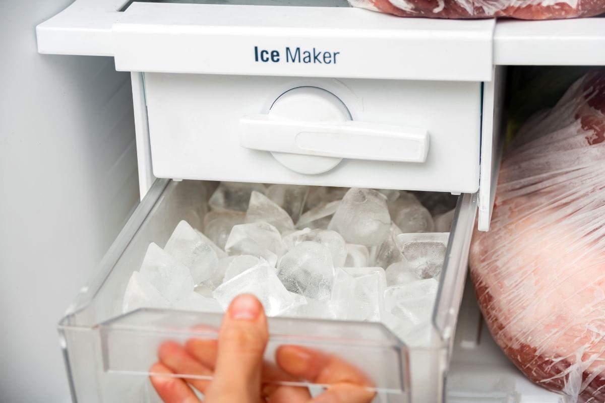 一名妇女打开冰箱里的制冰机托盘，取出冰块来冷却饮料。