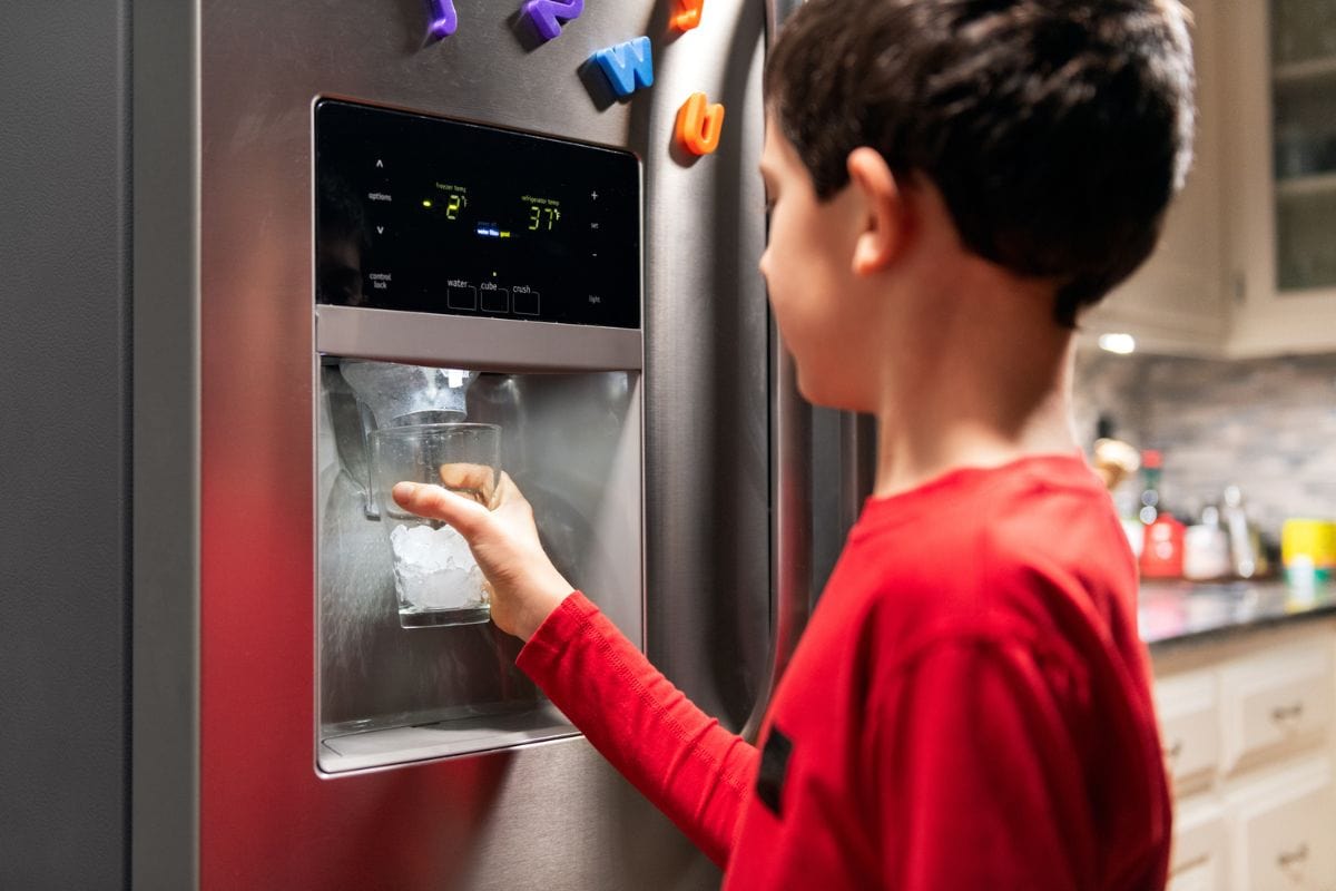 男孩从冰箱制冰机往玻璃杯里装冰块