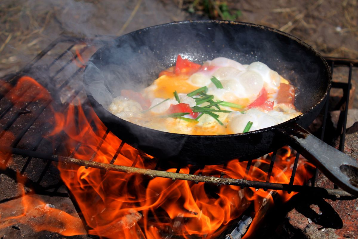 在森林里的营火上煎蛋，在野营旅行的营火上煎蛋，在火上用煎锅炒蛋，在火上做煎蛋卷，在营火上做饭，在火上吃早餐。